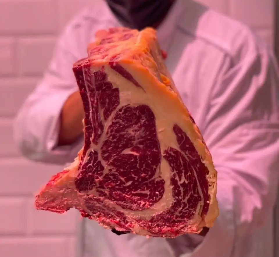 Il macellaio tiene in mano una costata frollata con il grasso ambrato